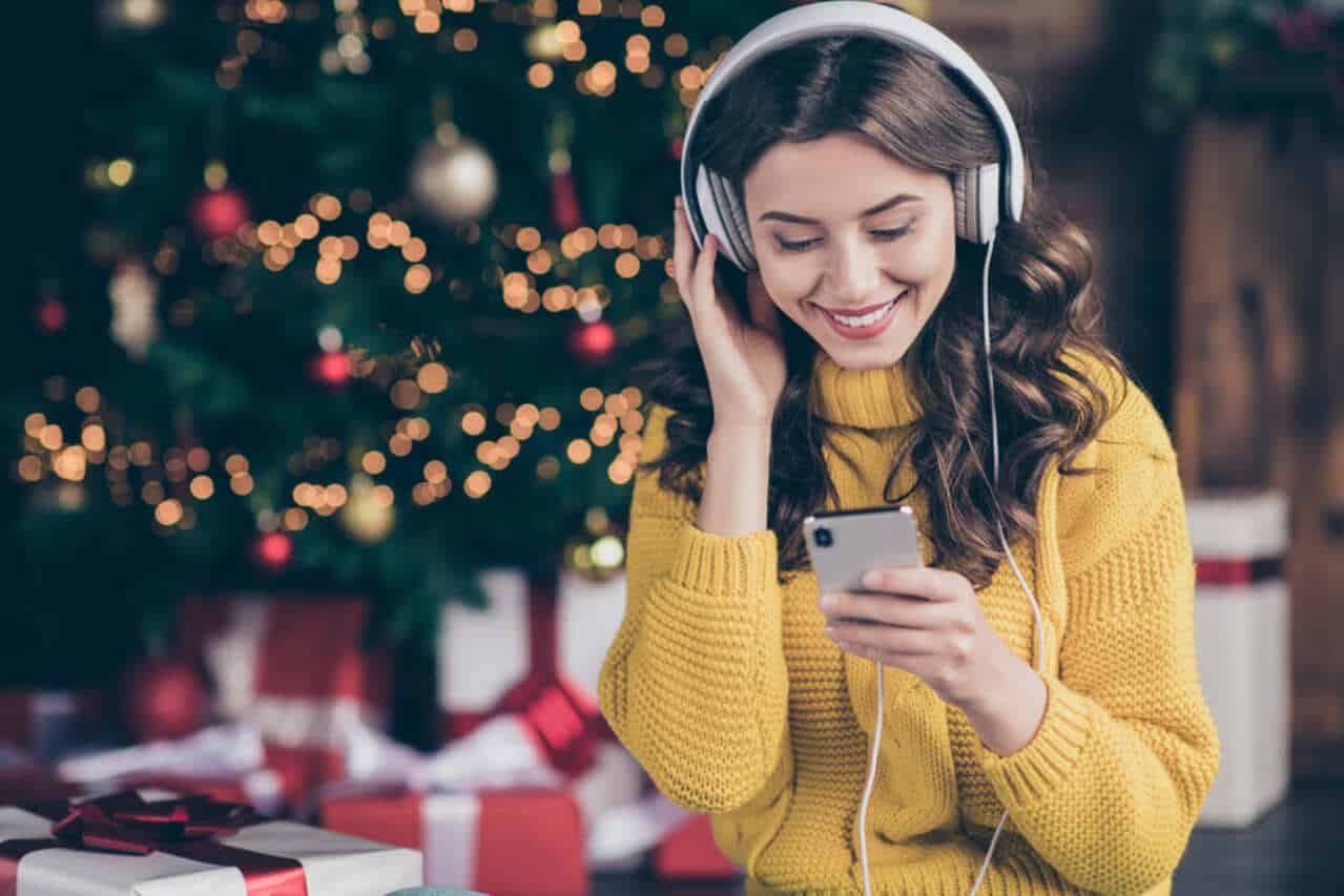 Smiling woman listening to music with headphones near Christmas tree