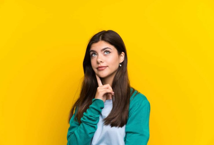 Young woman thinking with a bright yellow background