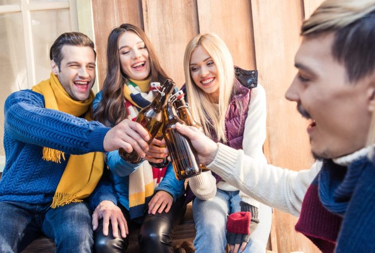 Group of friends toasting with beer bottles, laughing outdoors