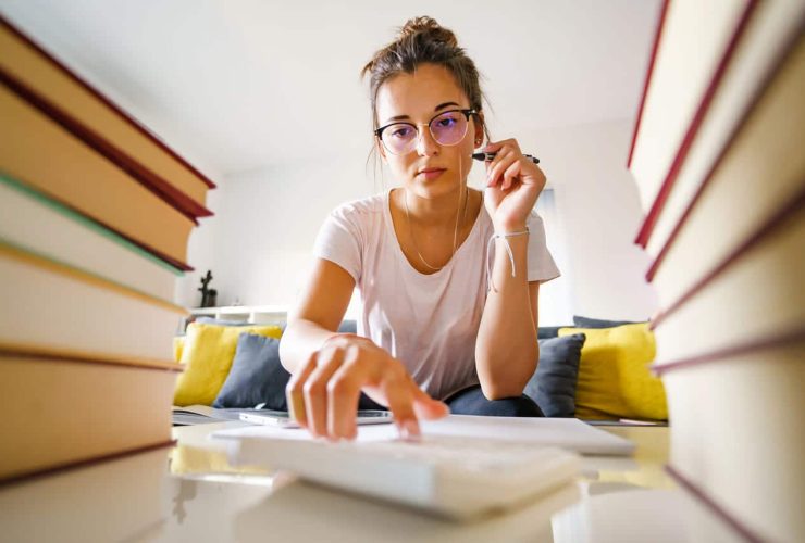 A woman studying, surrounded by books, using a calculator