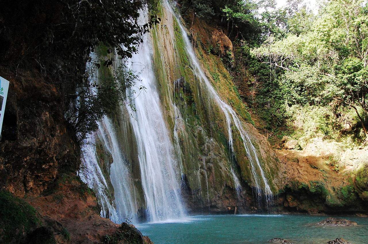 Waterfall cascading down a rocky cliff surrounded by greenery into a turquoise pool