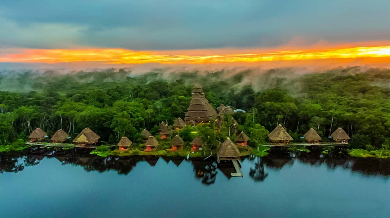 Aerial view of a forested area with huts near a river at sunset