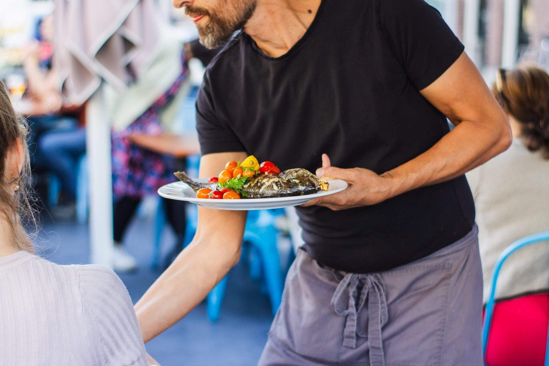 A waiter serves a plate of fish with vegetables at an outdoor restaurant