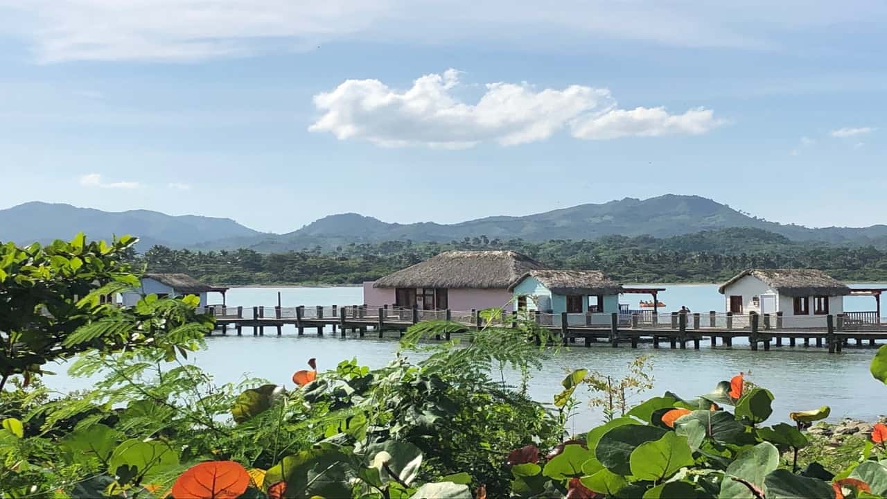 Overwater bungalows on a serene lake, surrounded by greenery and mountains