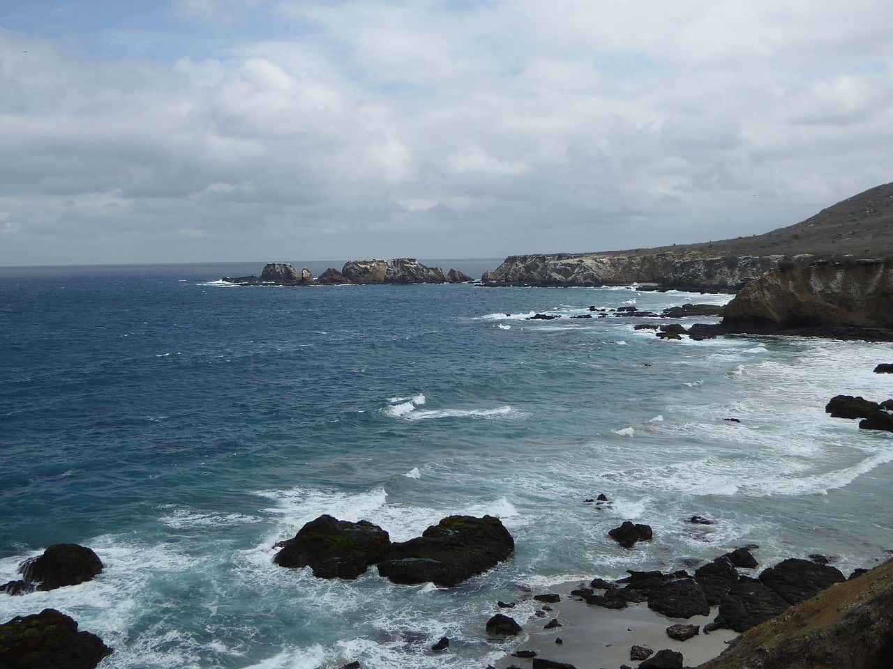 Coastline with rocky formations and waves crashing against them.