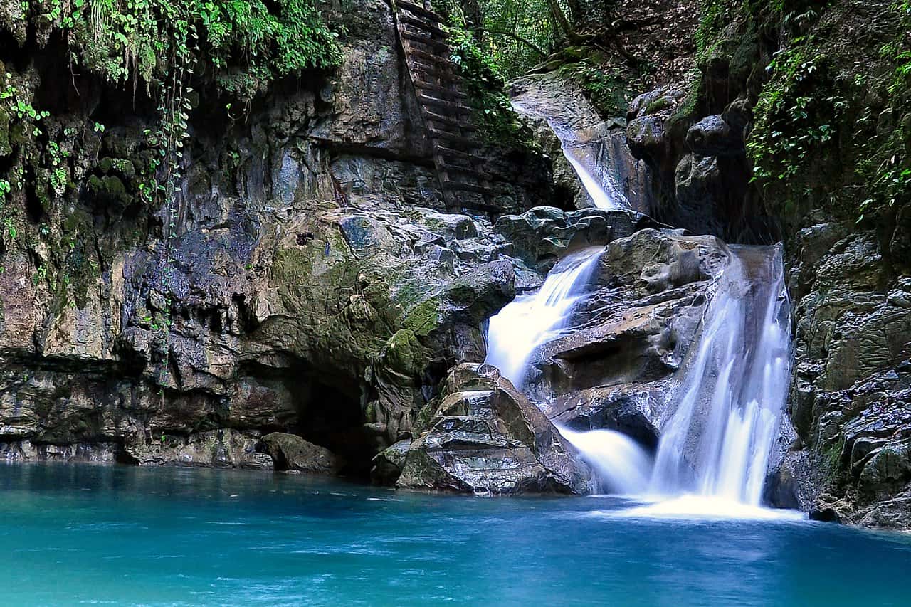 Small waterfall cascading into a clear blue pool surrounded by rocky terrain and lush vegetation