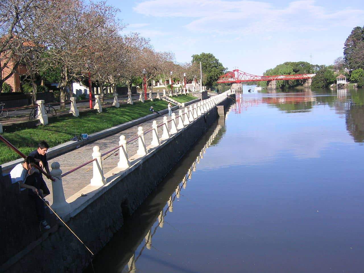 A calm river lined with a pedestrian pathway bordered by a low white stone railing