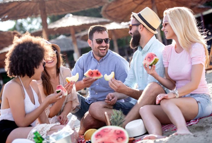 A group of friends enjoying watermelon at a beach picnic