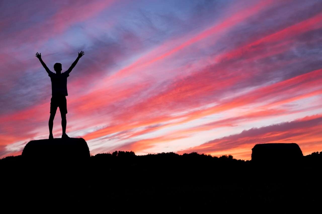 Silhouette of a person raising arms during sunset