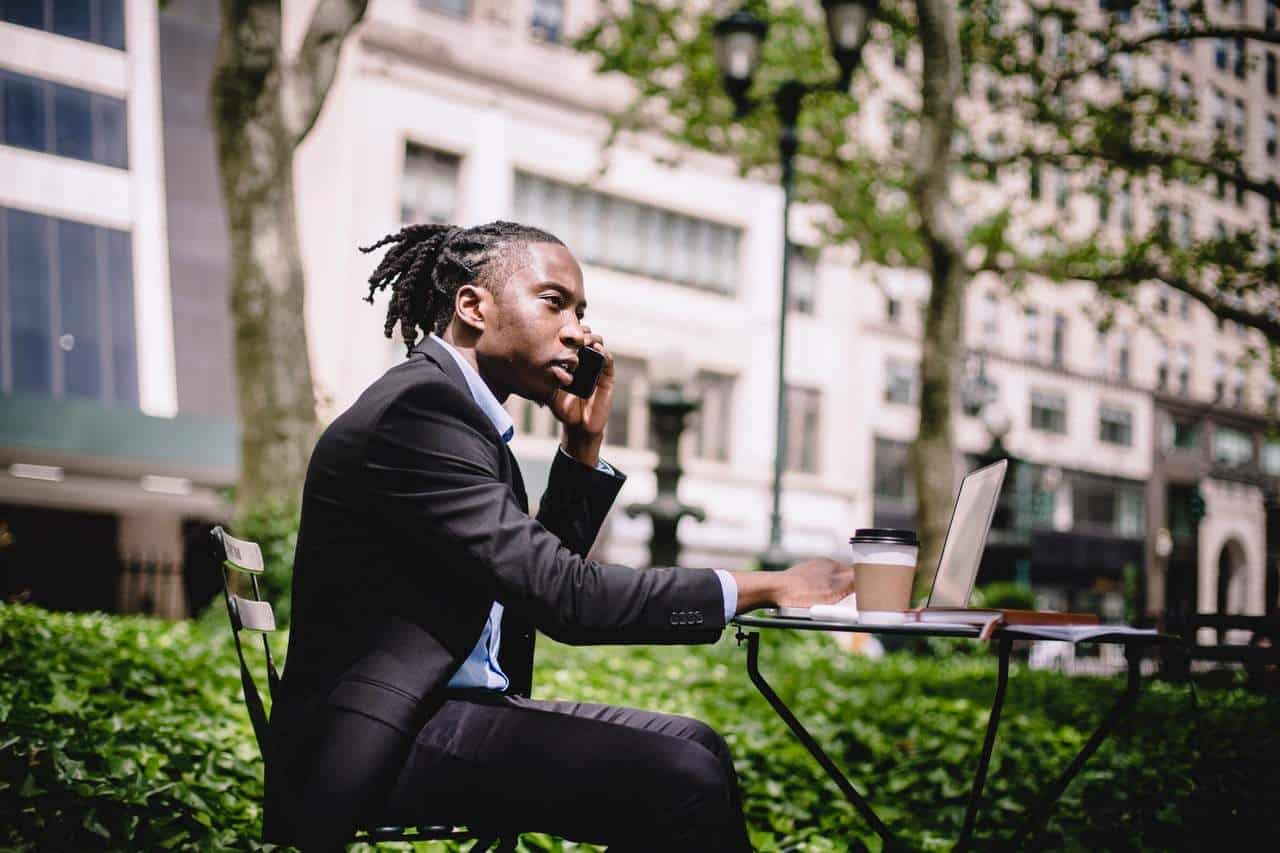 Man sitting outdoors using a laptop while on phone