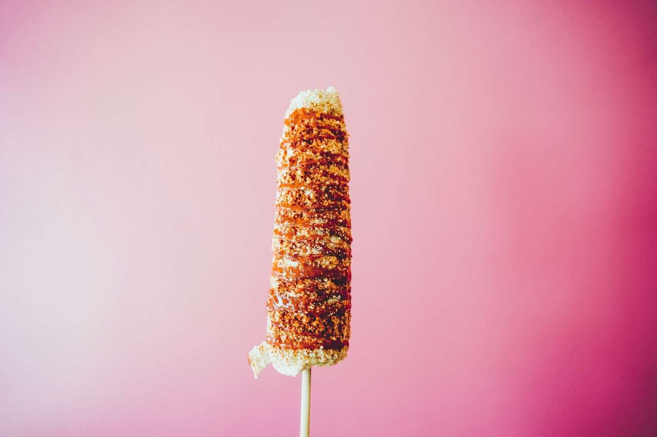 Grilled corn covered in spices against pink background