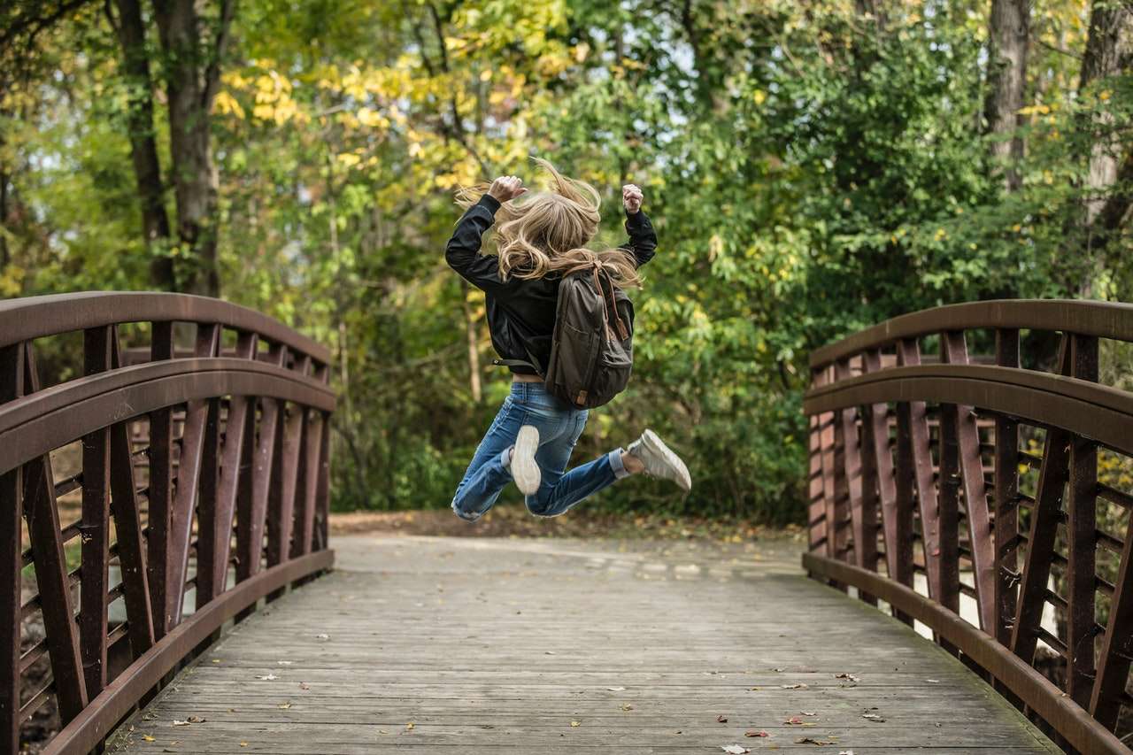 Person with backpack jumping on a bridge