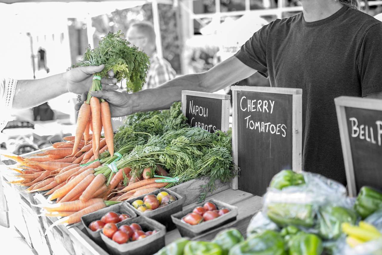 Person handing fresh carrots at a farmers market