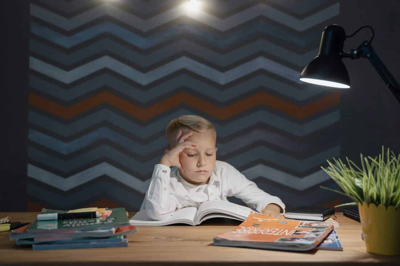 Boy reading a book under a desk lamp