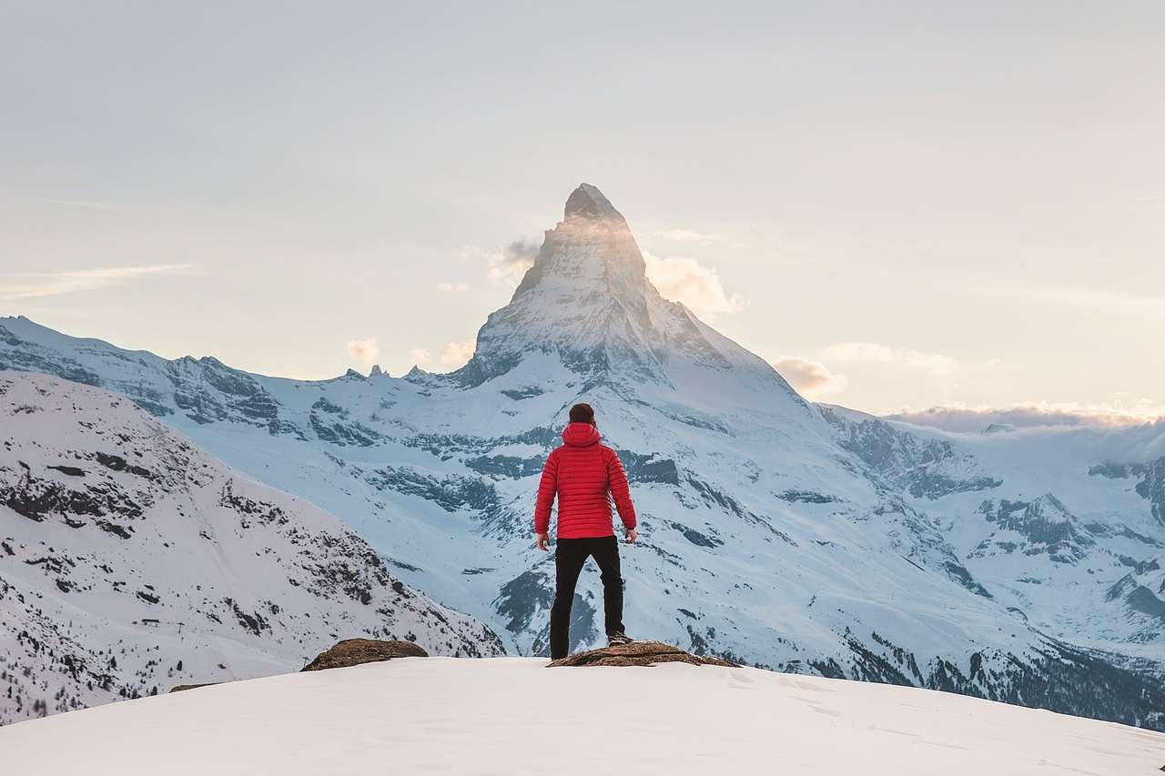 Person in a red jacket standing before a snowy mountain