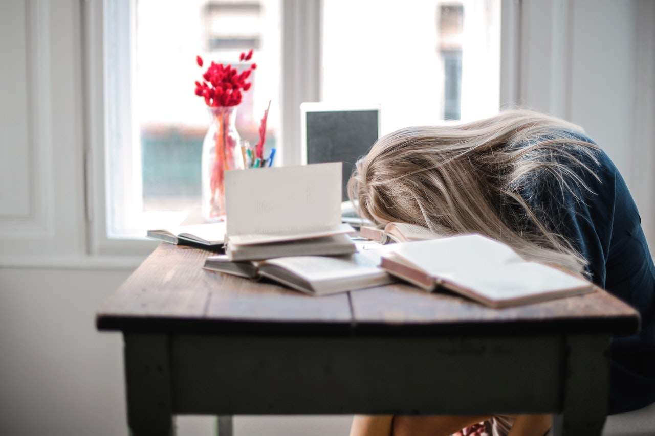 Person resting their head on a desk with books