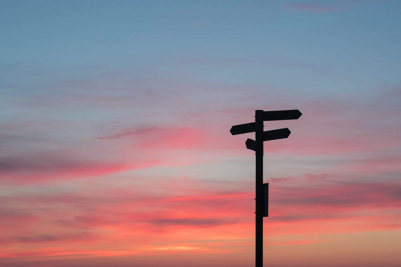 Signpost silhouette against a colorful sunset sky