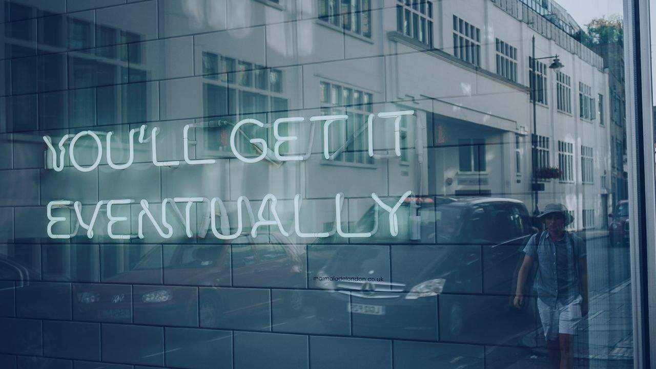 Glass window with neon sign reflecting buildings