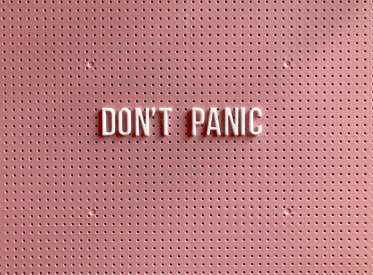 "Don't panic" text on a pink perforated board