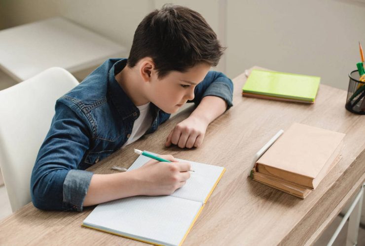 Young boy focused on writing in a notebook at desk