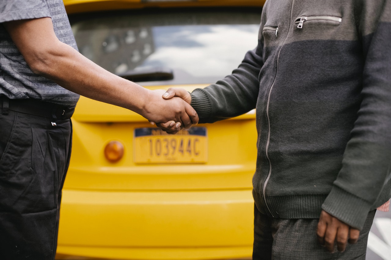 Two people shaking hands in front of yellow car