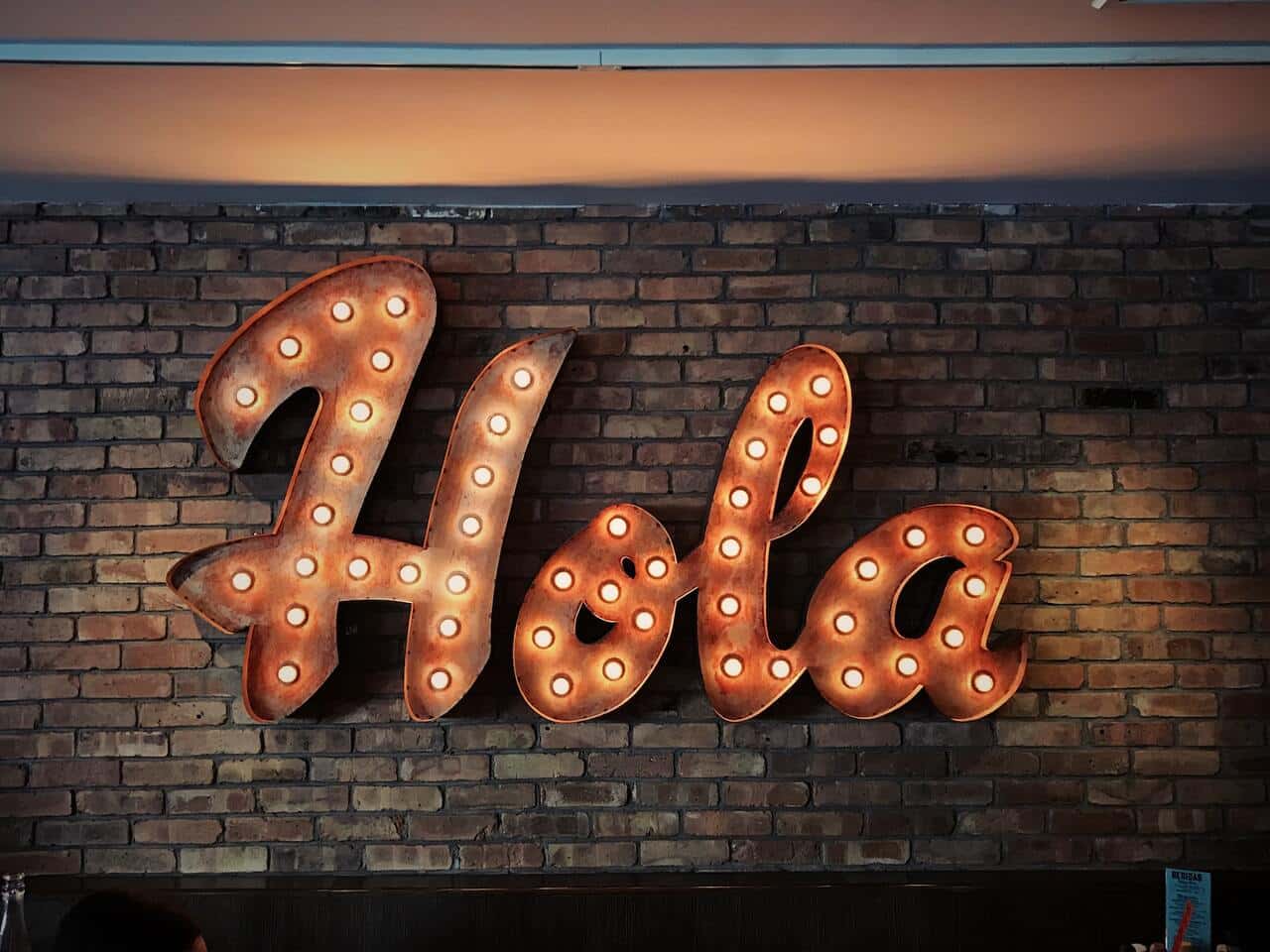 Illuminated "Hola" sign on a brick wall