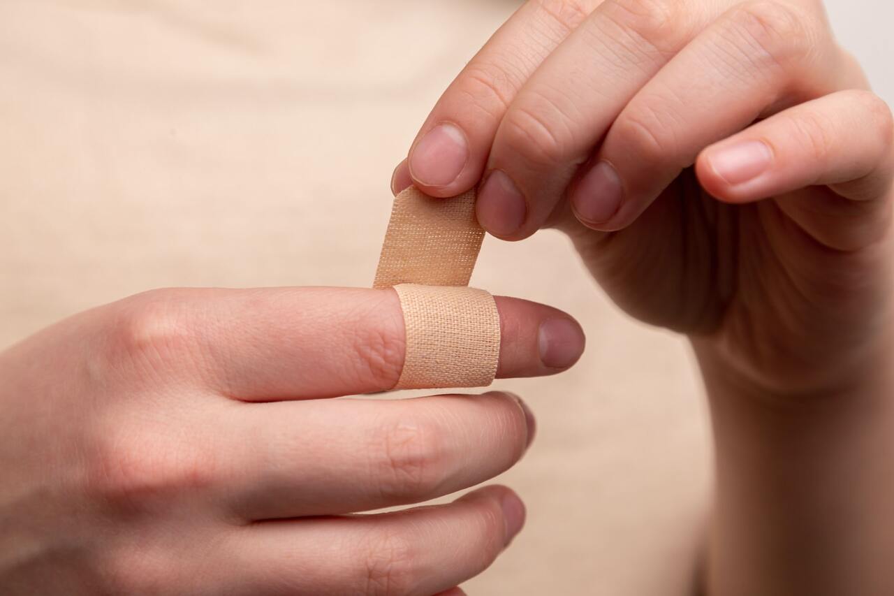 A person is applying a beige bandage around their finger