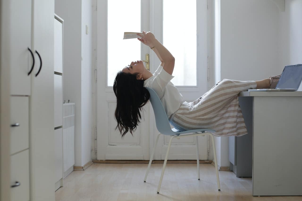 Woman leaning back in chair while reading a book