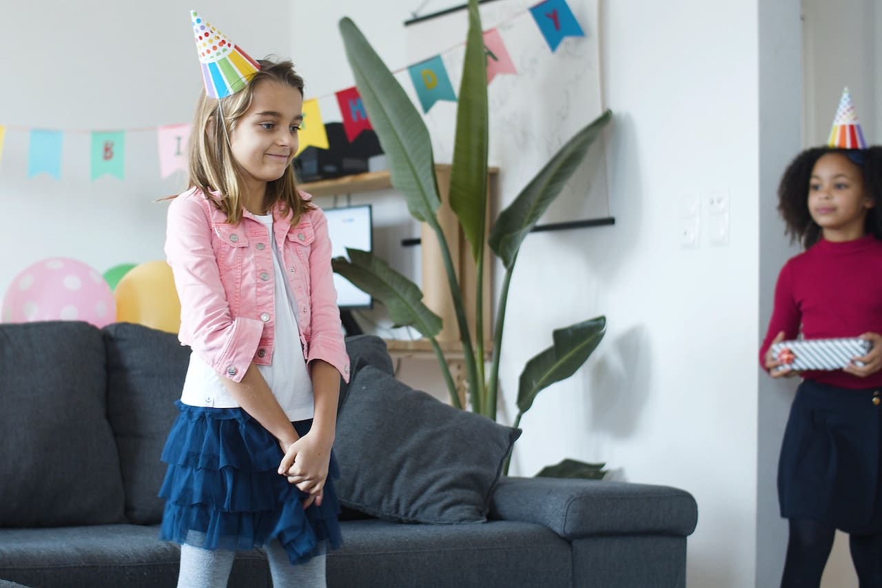 Young girl wearing a party hat, standing at a birthday party.