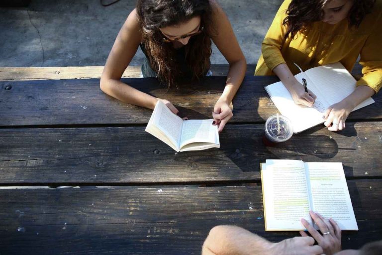 People sitting outdoors reading and taking notes at a table