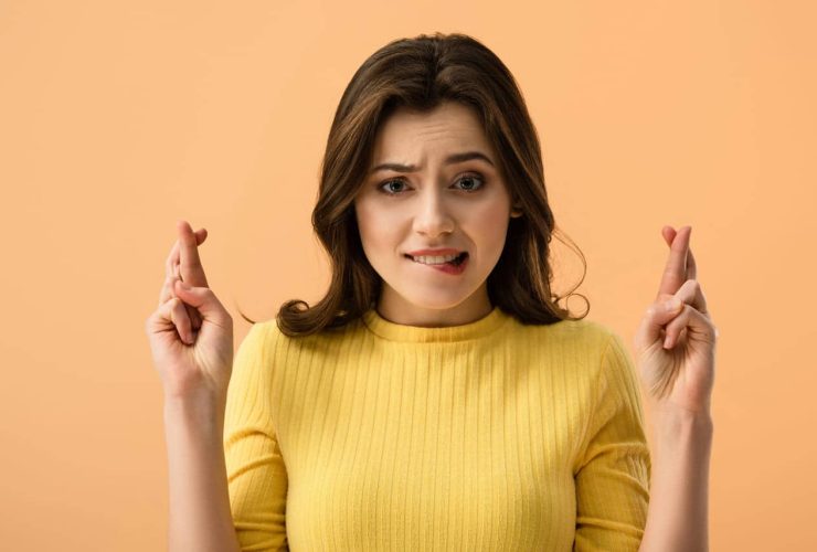 Woman with crossed fingers, looking nervous, in a yellow top