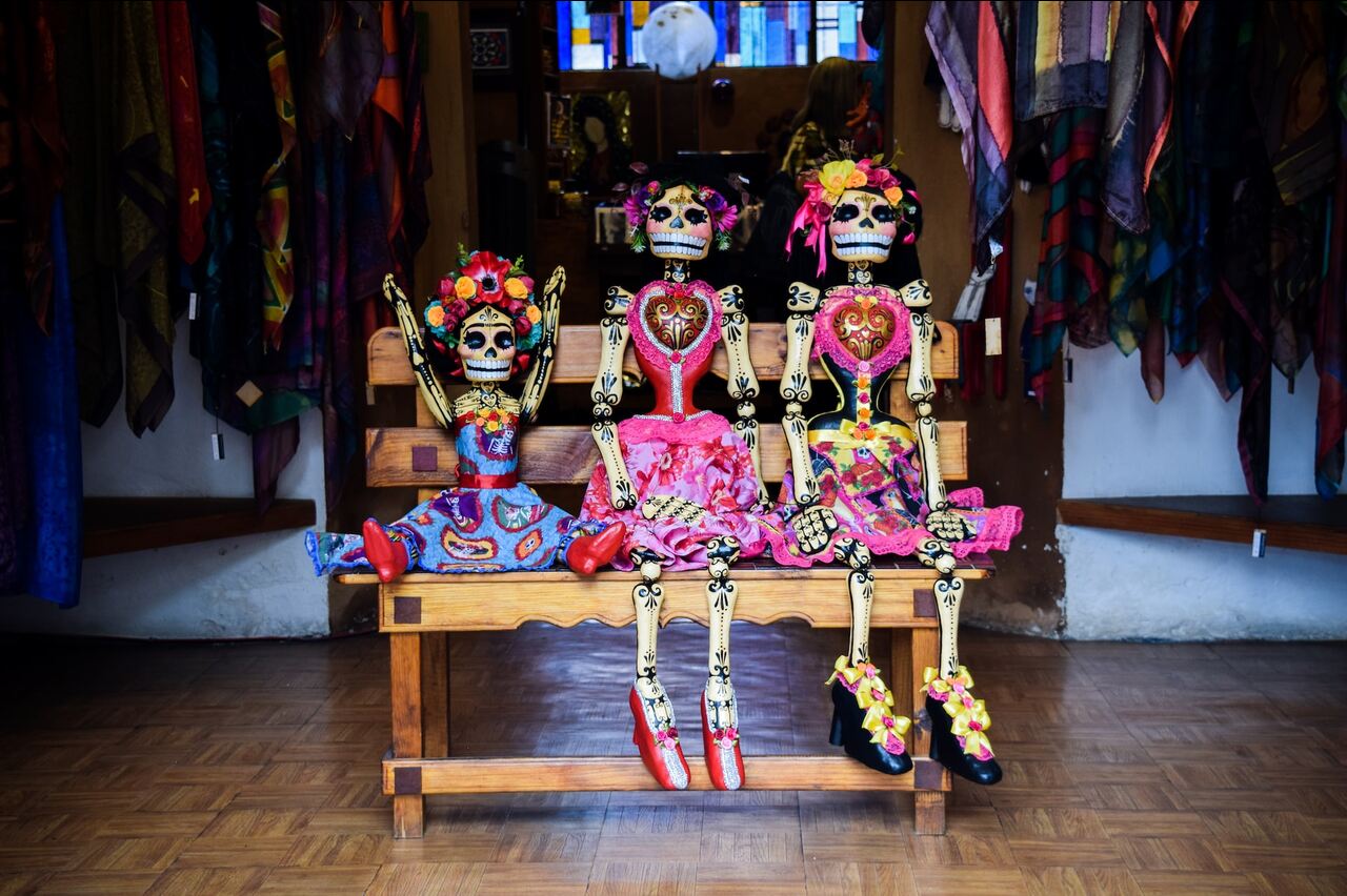 Three colorful skeleton dolls sitting on a wooden bench