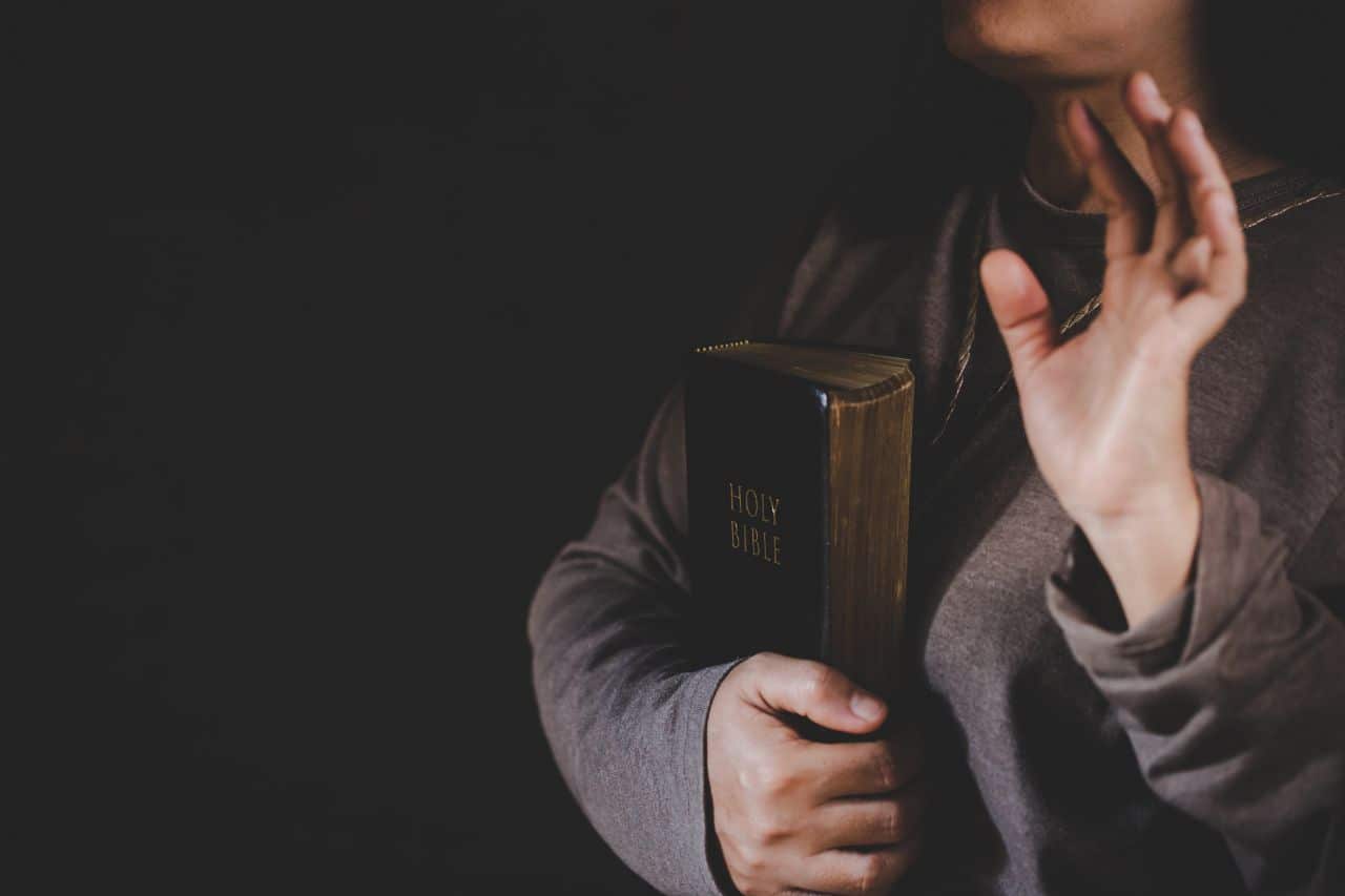 Person holding a Holy Bible with one hand raised