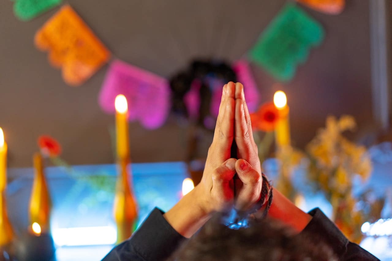 Hands in prayer with candles and colorful decorations