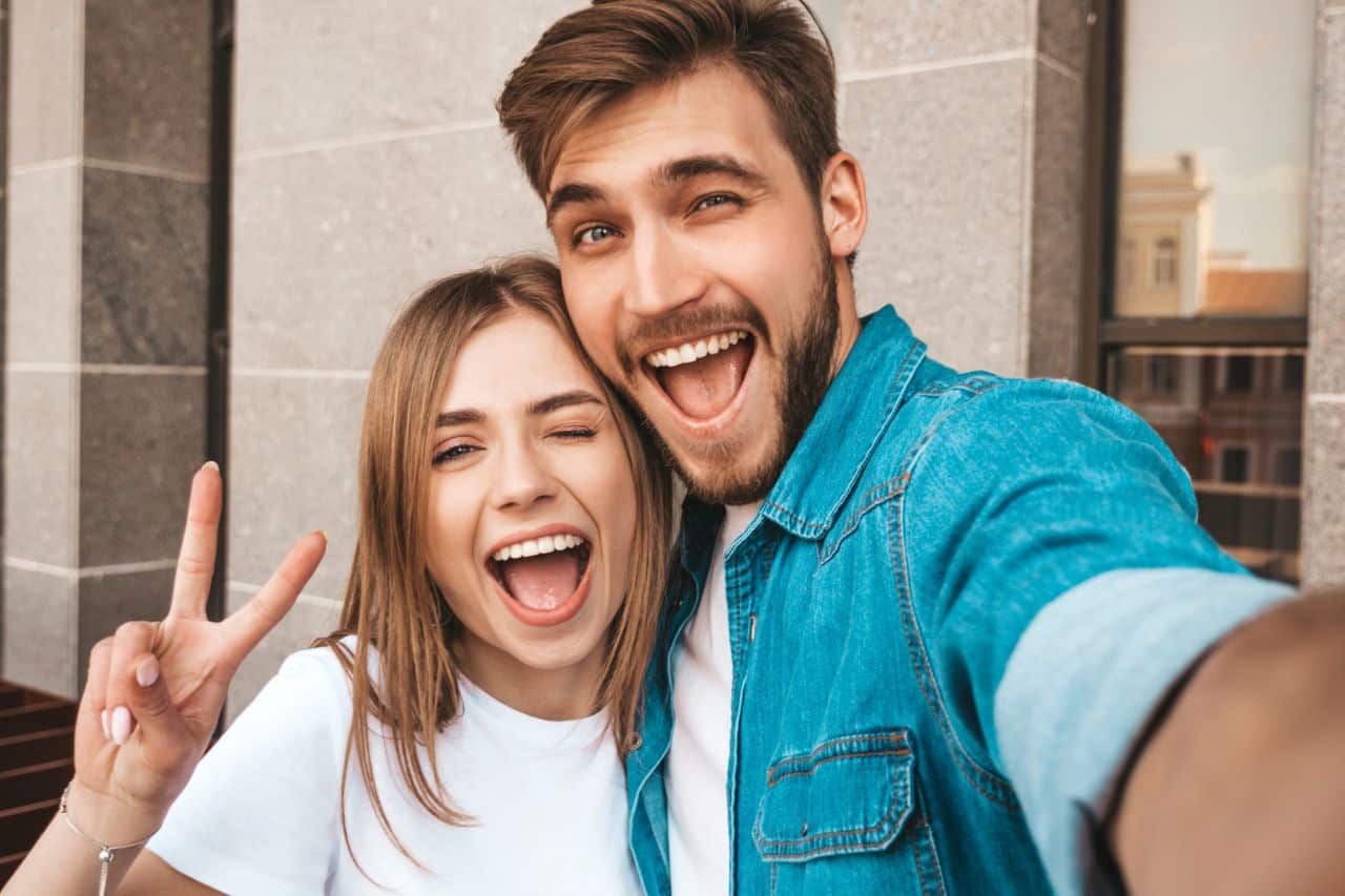 A happy couple taking a selfie together, smiling and making fun expressions.