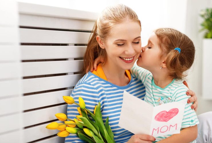 Child kissing mother holding flowers and card