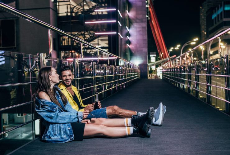 Couple sitting on a bridge at night, smiling