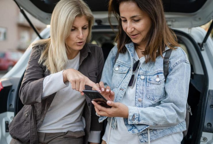 Two women looking at a smartphone near a parked car