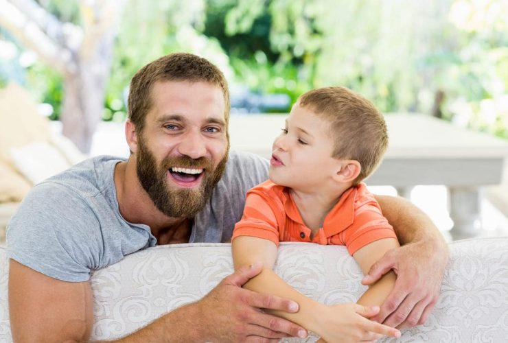 A father and son smiling together on a couch