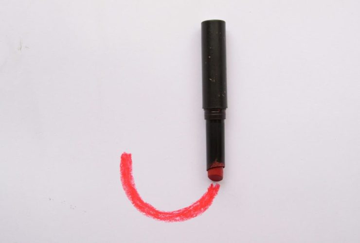 Lipstick drawing a red curve on a white surface.