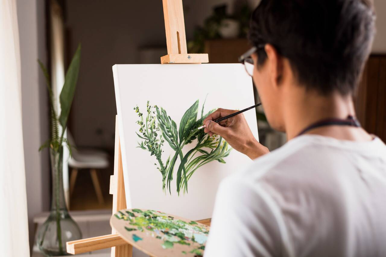 Person painting green leaves on canvas with a palette