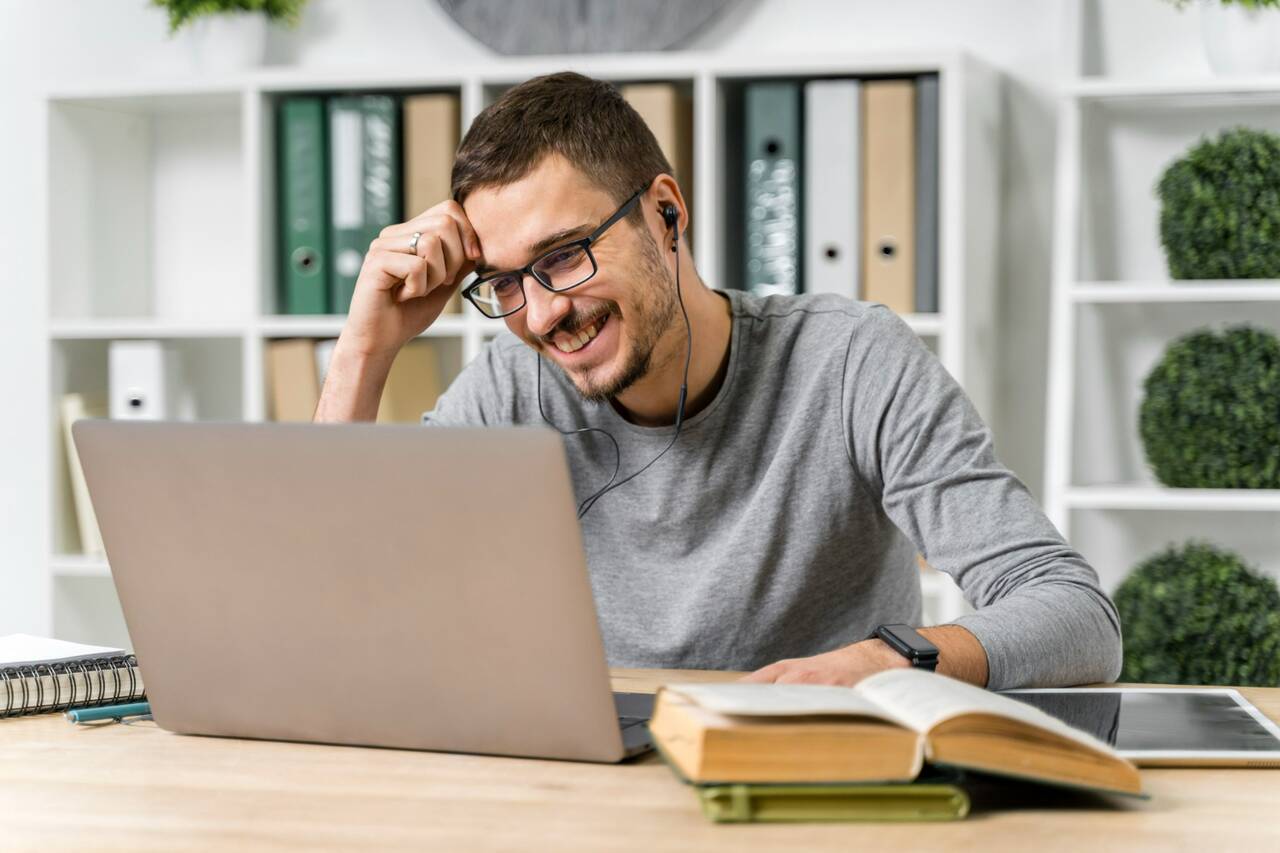 Man smiling while studying on laptop wearing earphones