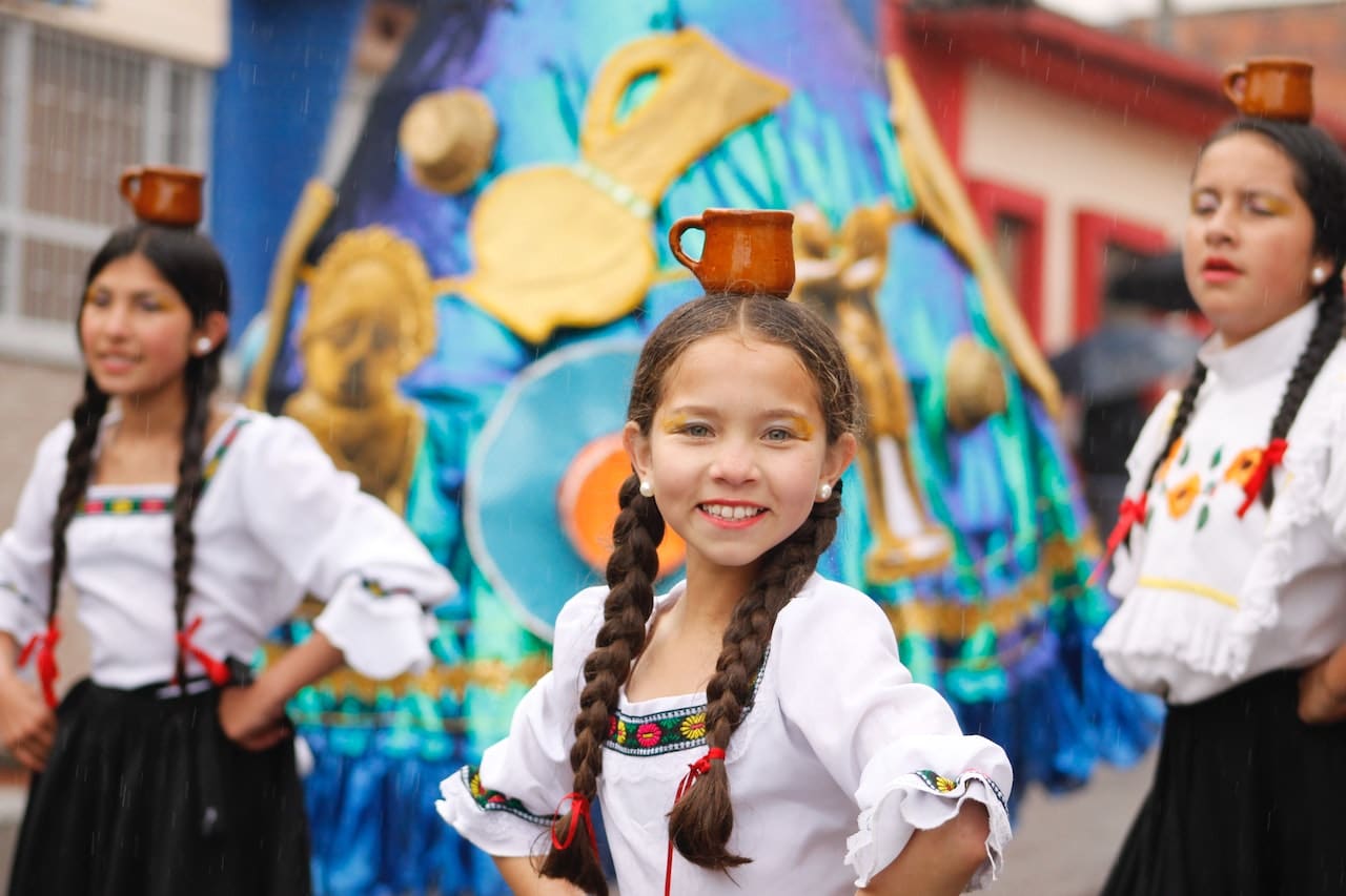 young girls in traditional outfits balancing cups on heads