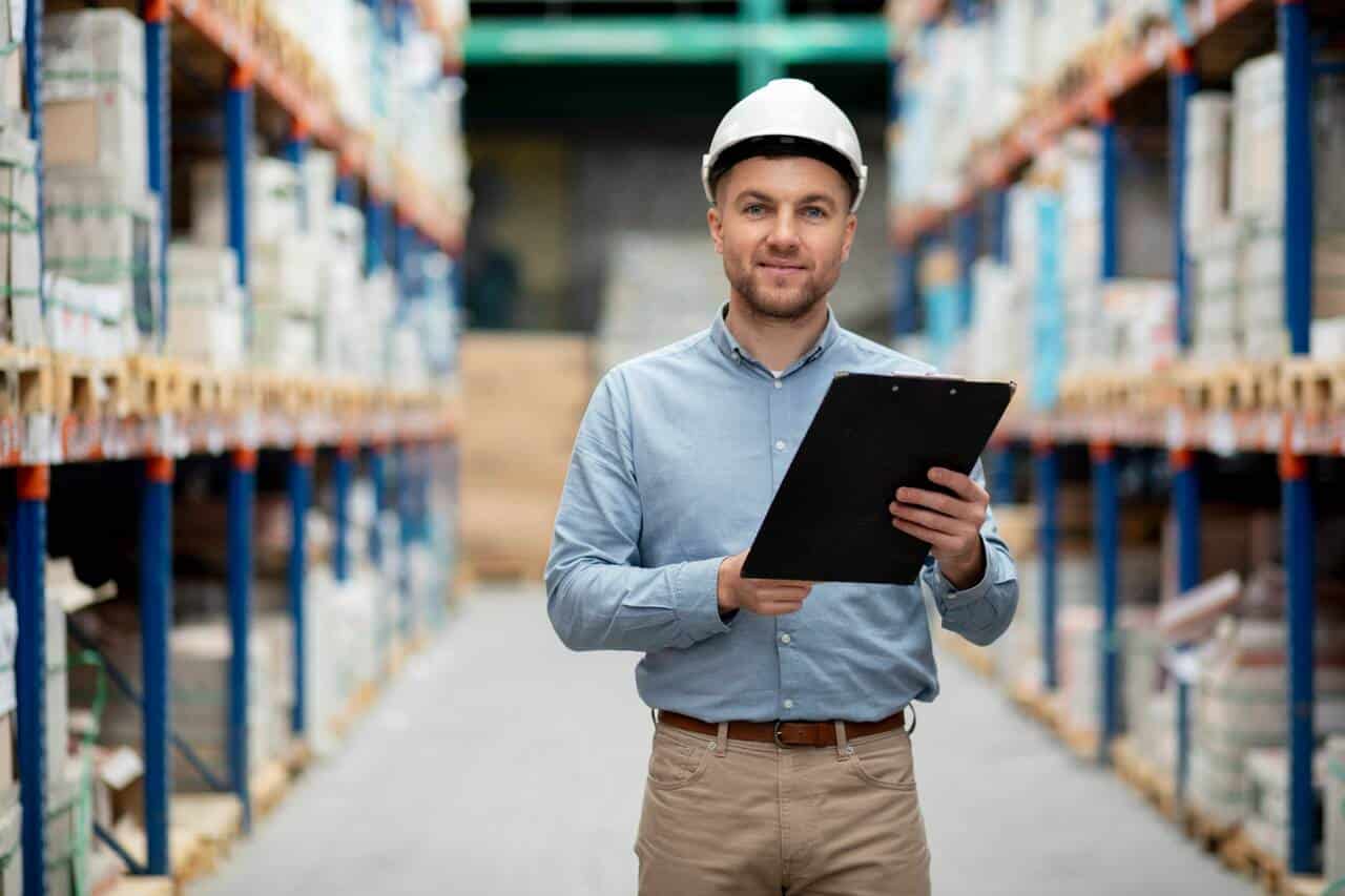 Man wearing a hard hat holding a clipboard in a warehouse