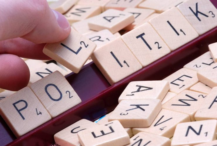 Hand placing Scrabble tiles to spell "POLITIK" on a game board