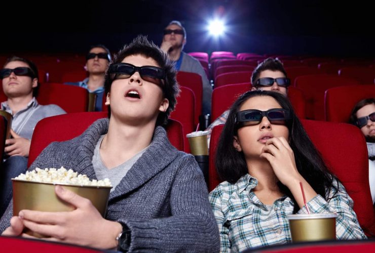 People in a theater wearing 3D glasses, eating popcorn.