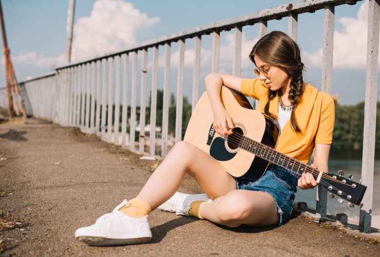 A woman sitting by a railing, playing an acoustic guitar