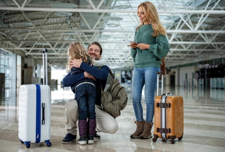 Father hugging child at an airport, mother smiling nearby