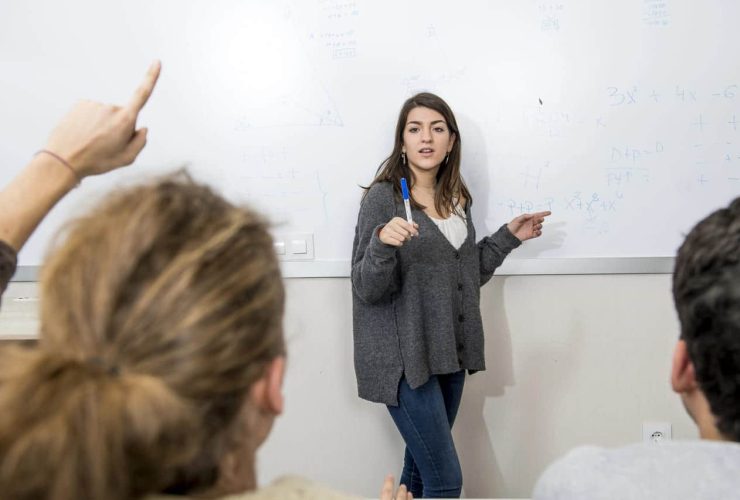 A teacher explains a concept at a whiteboard to students.