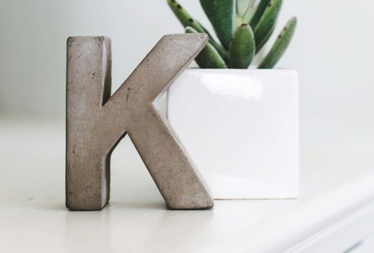 Concrete "K" next to a white potted plant.